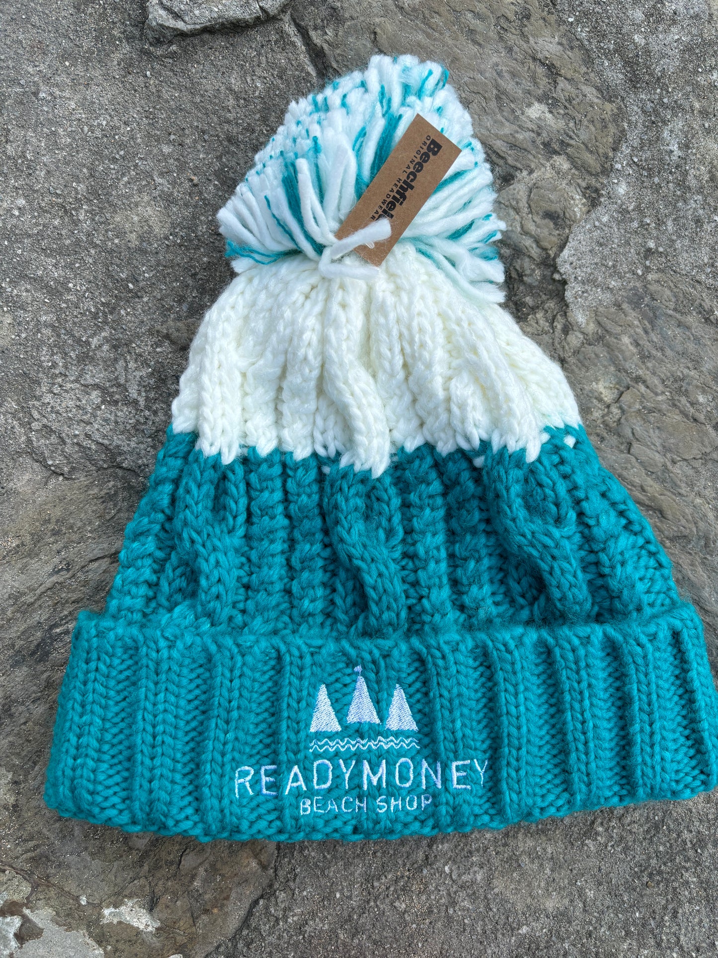 turquoise-white chunky bobble hat with faux fur pom-pom and beach shop logo—cozy, vibrant, and winter-ready for kids