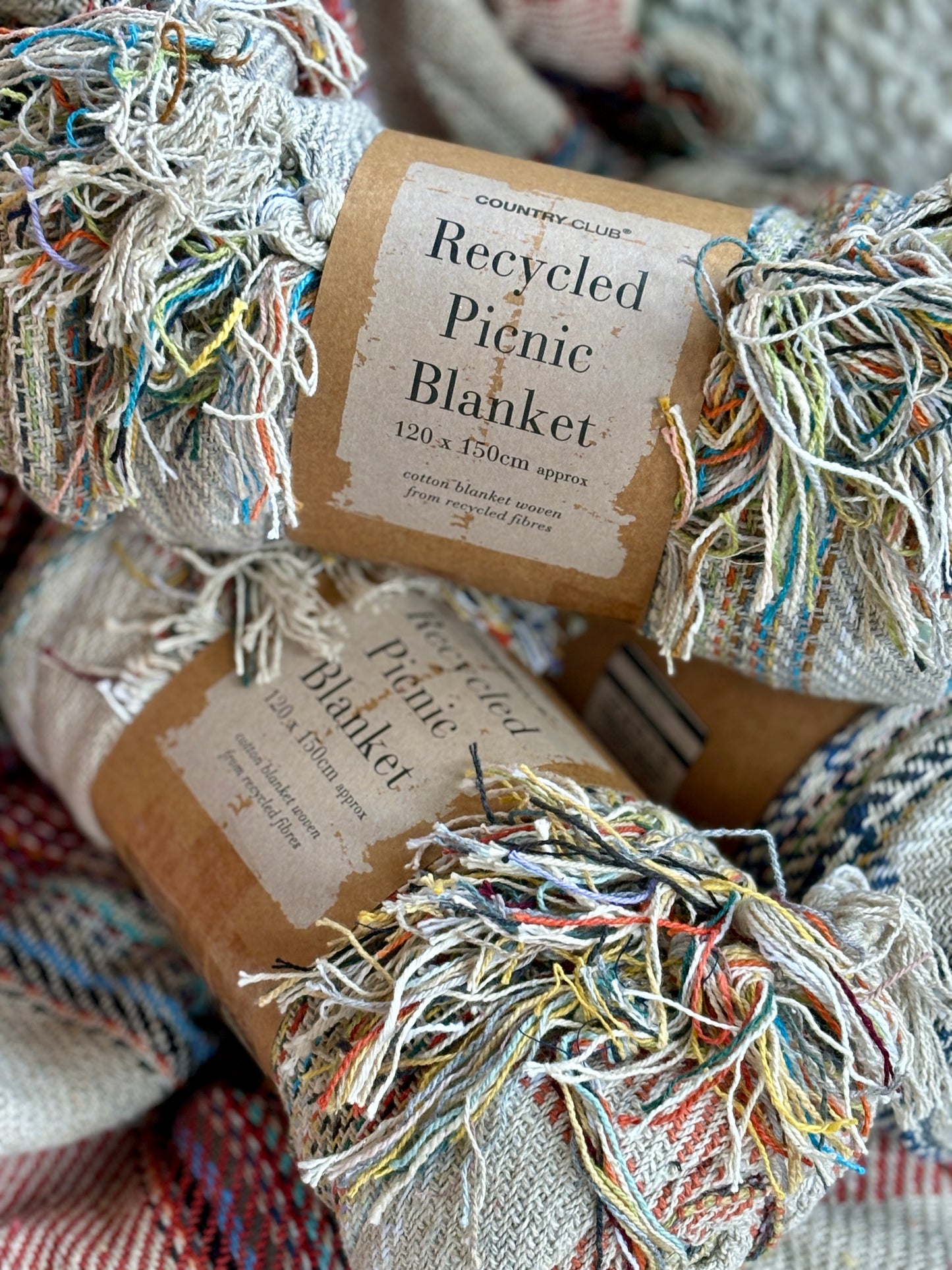 closeup shot of three rolled, recycled cotton picnic blankets sustainable, eco-friendly throw, woven from multi-coloured recycled fibres