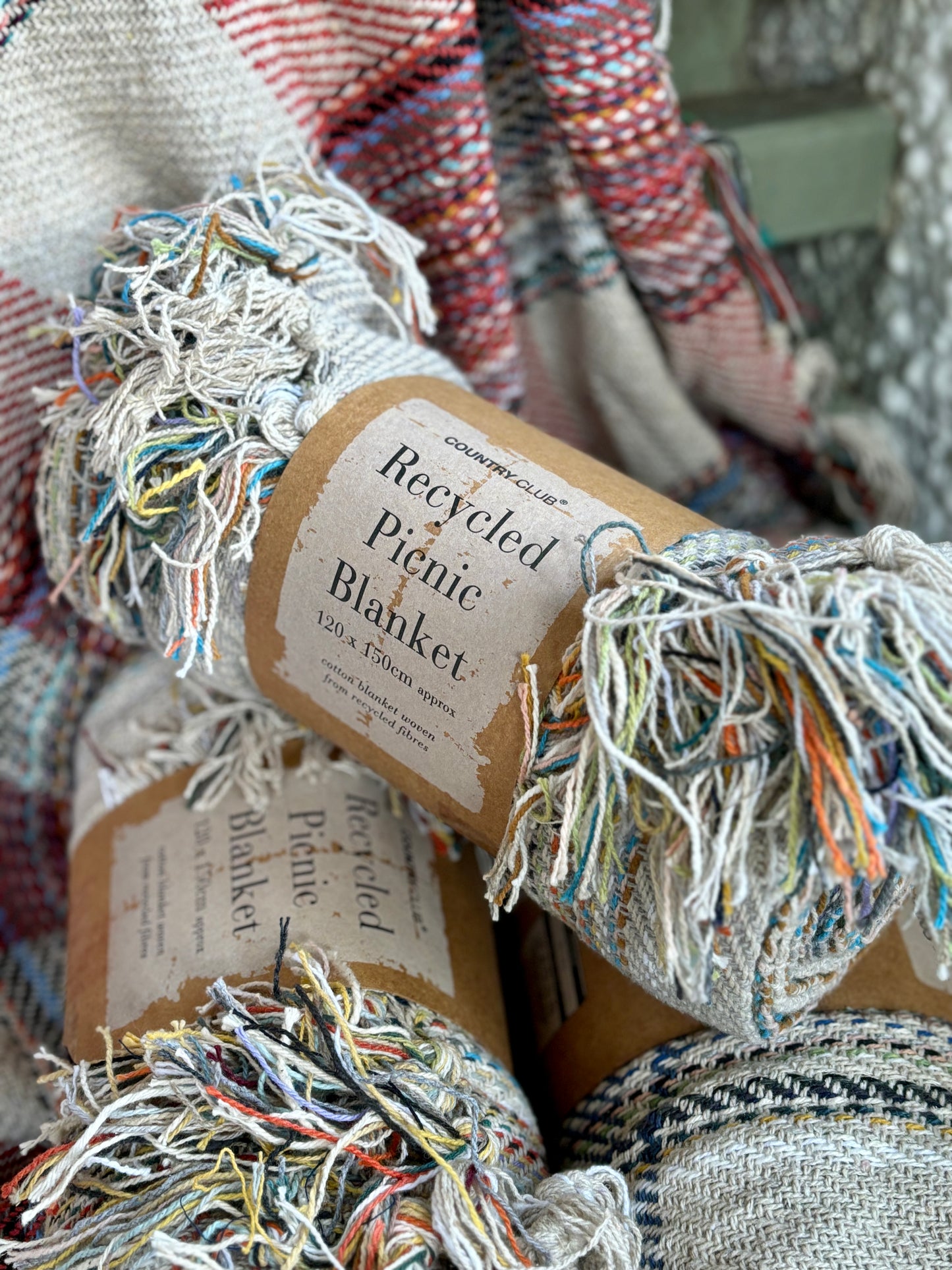 closeup shot of three rolled, recycled cotton picnic blankets sustainable, eco-friendly throw, woven from multi-coloured recycled fibres
