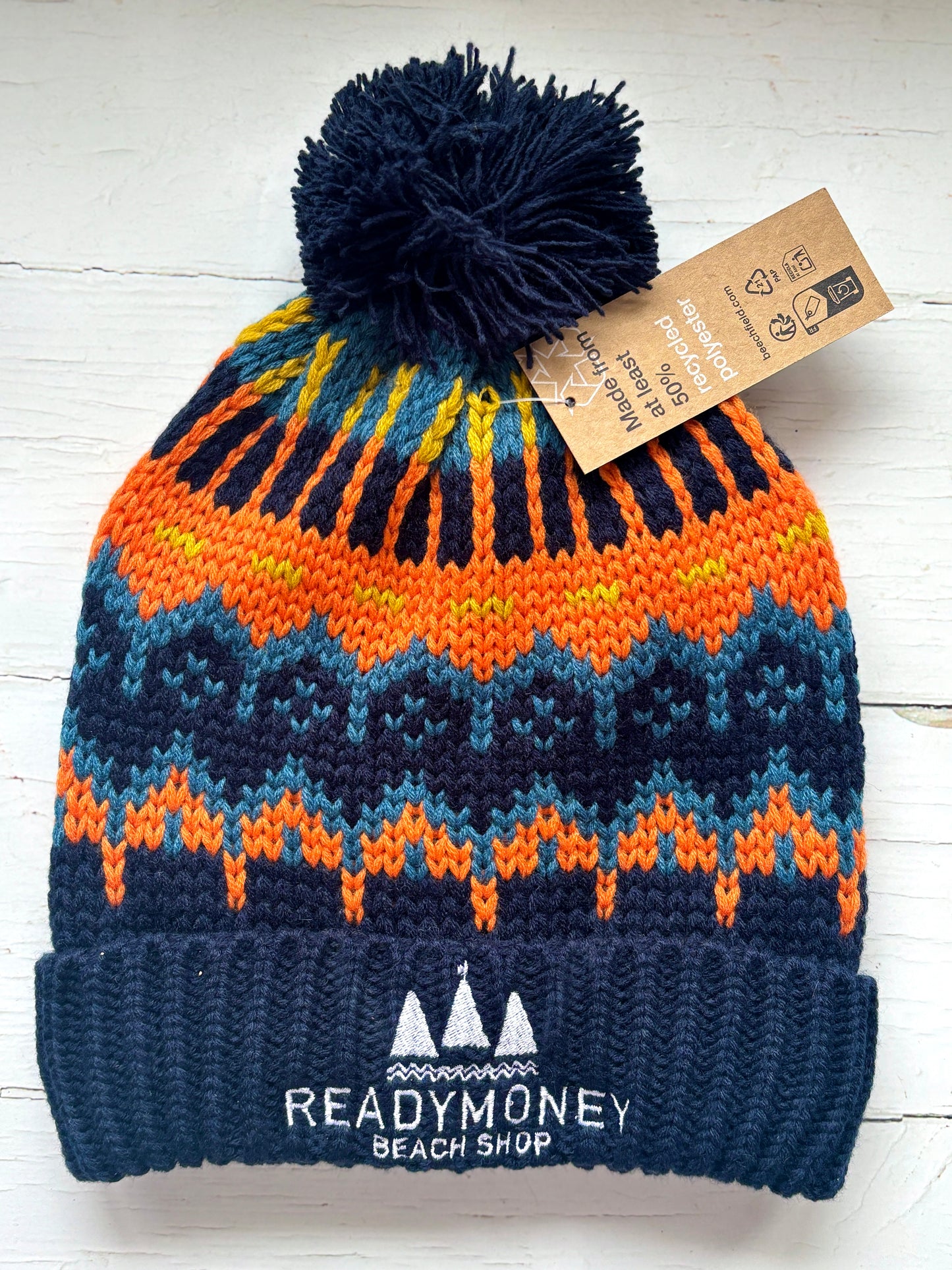 retro knit bobble hat with navy ribbed brim, bold orange-yellow zigzag pattern, and beach shop logo—eco-friendly winter style