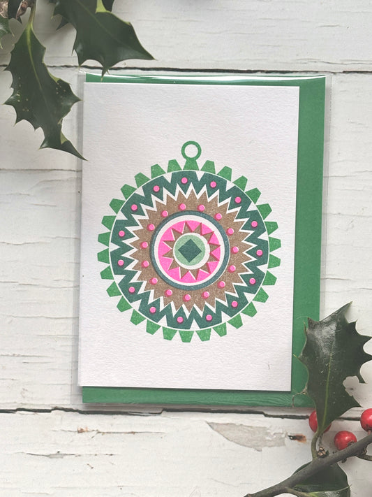 retro-style bauble card—bold geometric Christmas ornament in pink, green, and gold on white card with holly, ideal for festive gifting