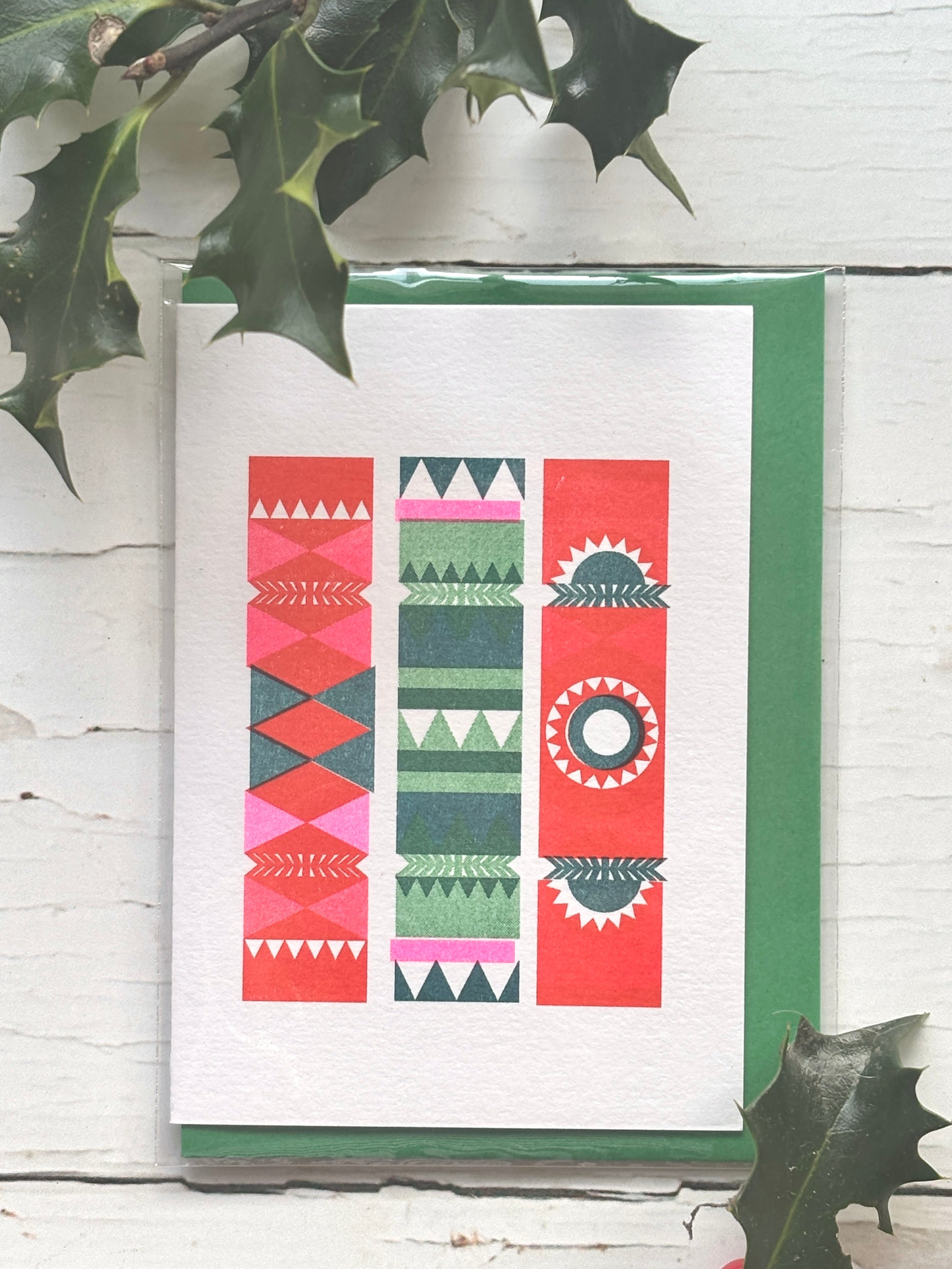 retro style Christmas card with three colorful crackers in red, green, and pink geometric design, festive holly decor