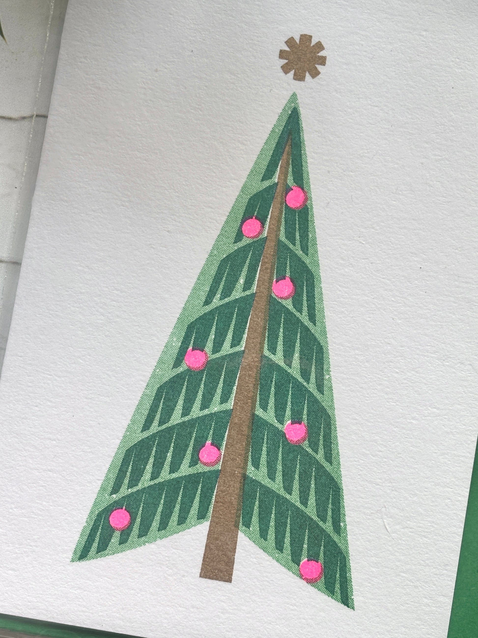 closeup shot of retro style Christmas card with minimalist green tree, pink baubles, and gold star, festive modern design