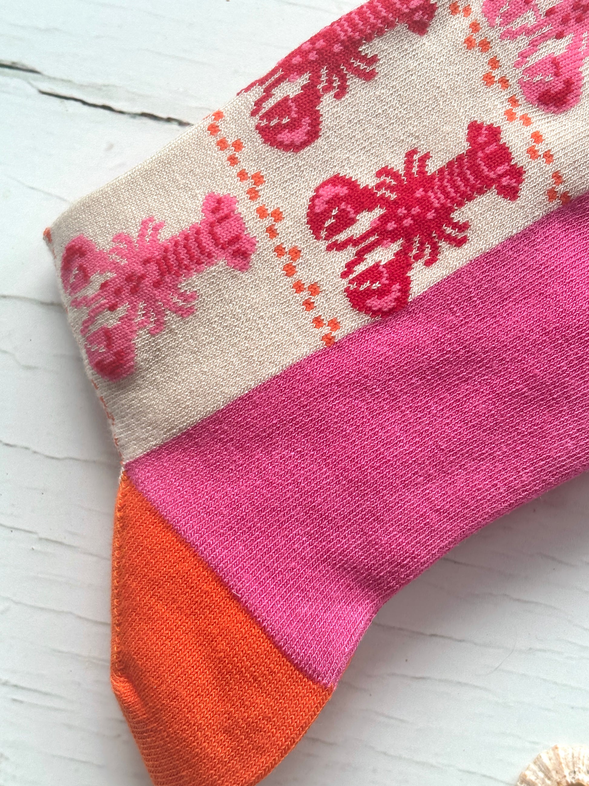 closeup shot of Sock Talk bamboo socks with a knitted lobster pattern, pink band, and bright orange toe coastal apparel gift idea