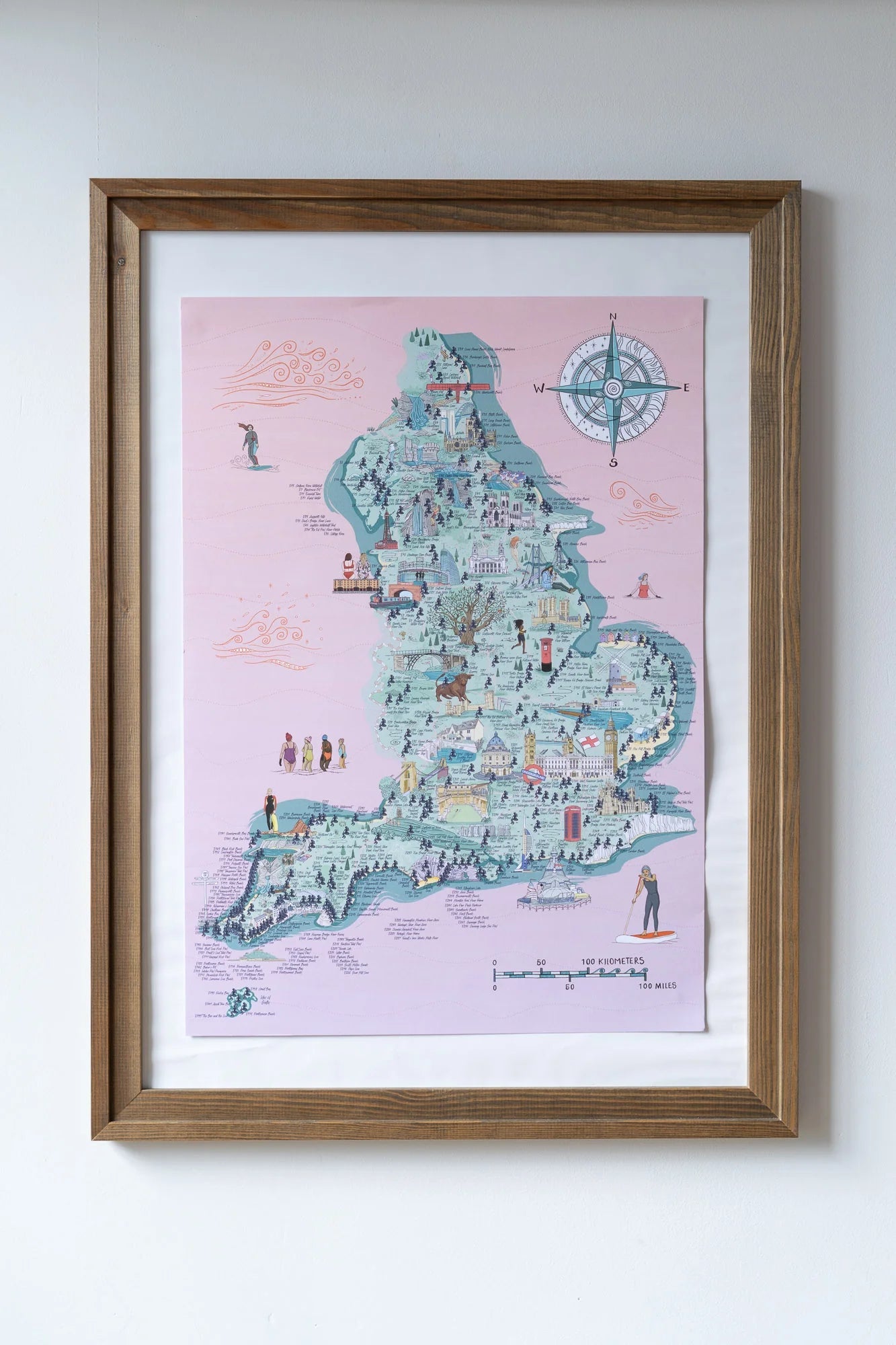 framed England swim map poster with pink background, whimsical landmarks, and coastal-themed wall art