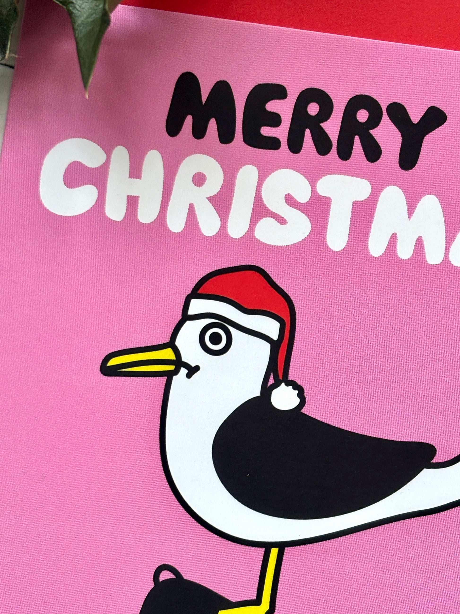 Close-up festive seagull Christmas card with Santa hat and “Merry Christmas” text on pink background, holiday greeting design