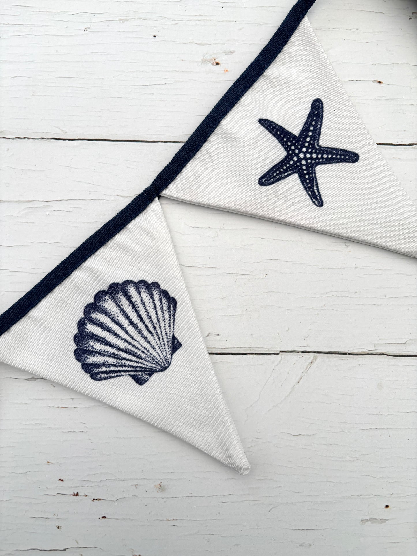 closeup shot of white cotton bunting with navy seashell and starfish print—coastal fabric garland for beach-themed decor