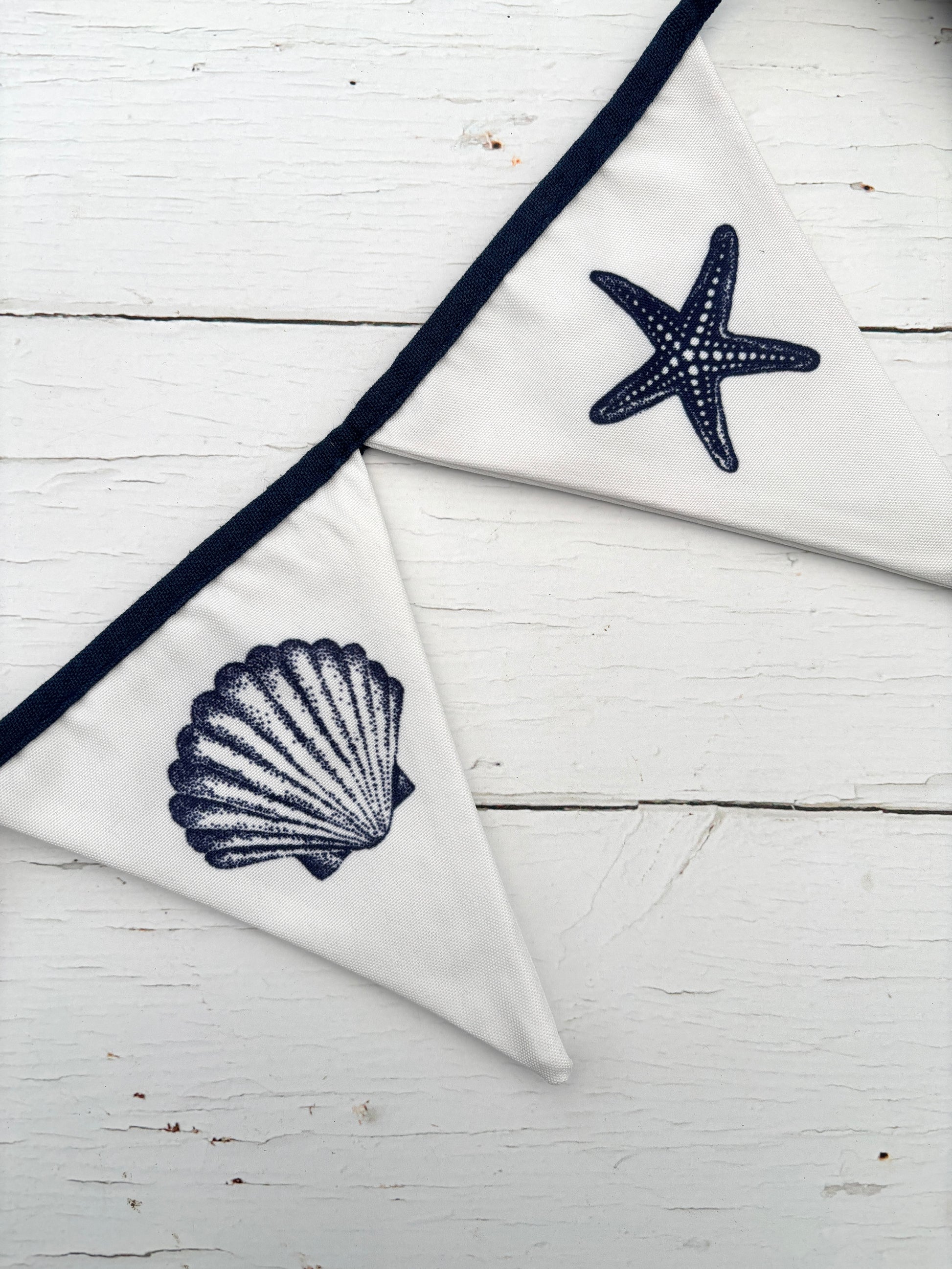 closeup shot of white cotton bunting with navy seashell and starfish print—coastal fabric garland for beach-themed decor