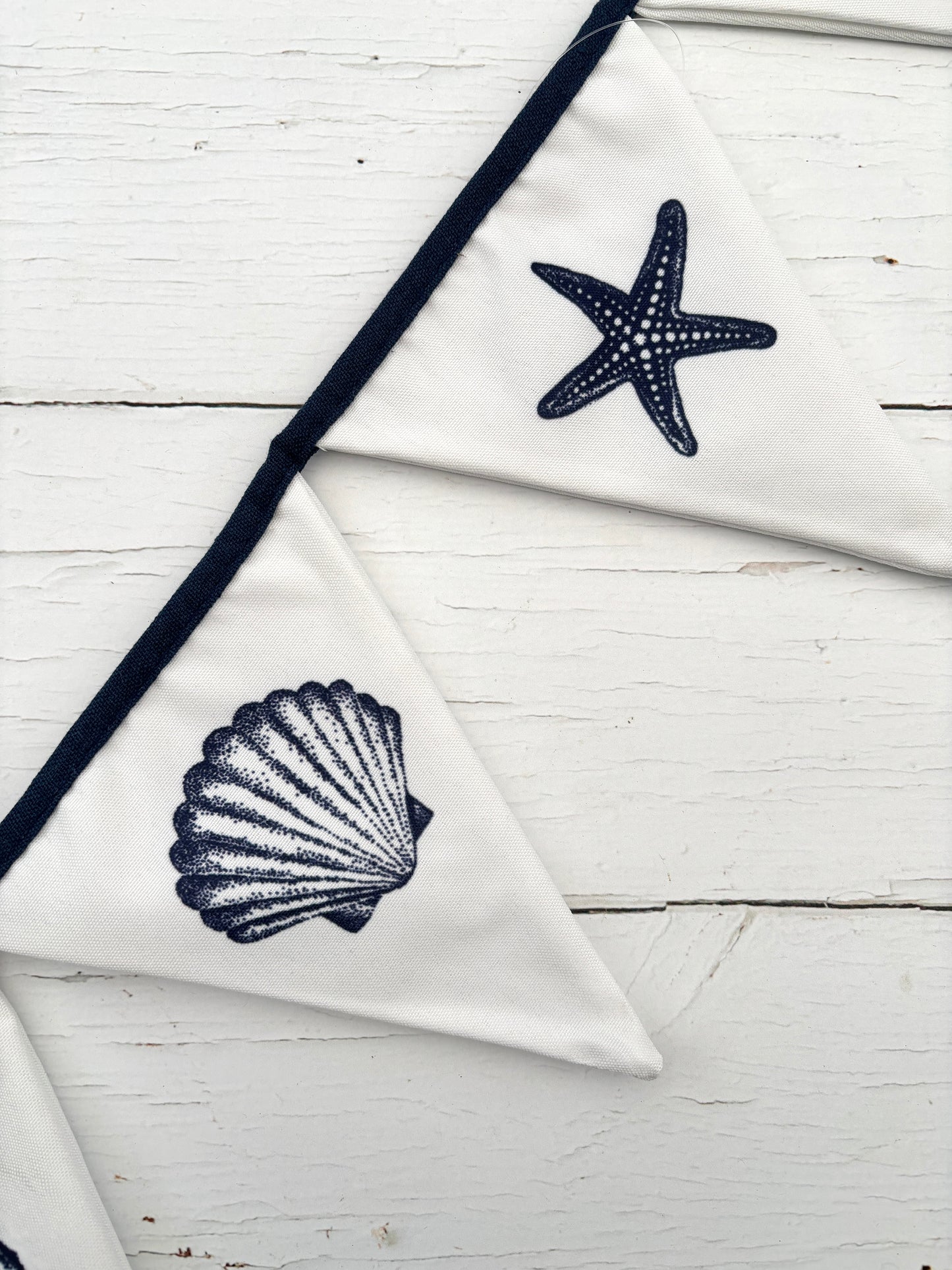 closeup shot of white cotton bunting with navy seashell and starfish print—coastal fabric garland for beach-themed decor
