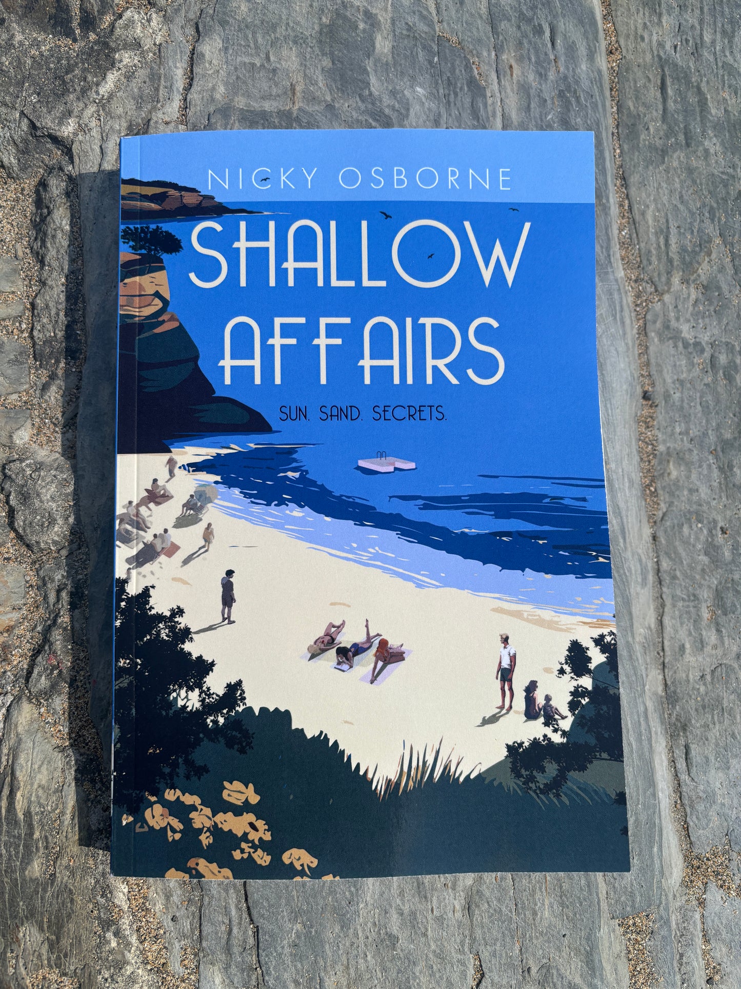 Book titled 'Shallow Affairs' by Nicky Osborne on a stone surface