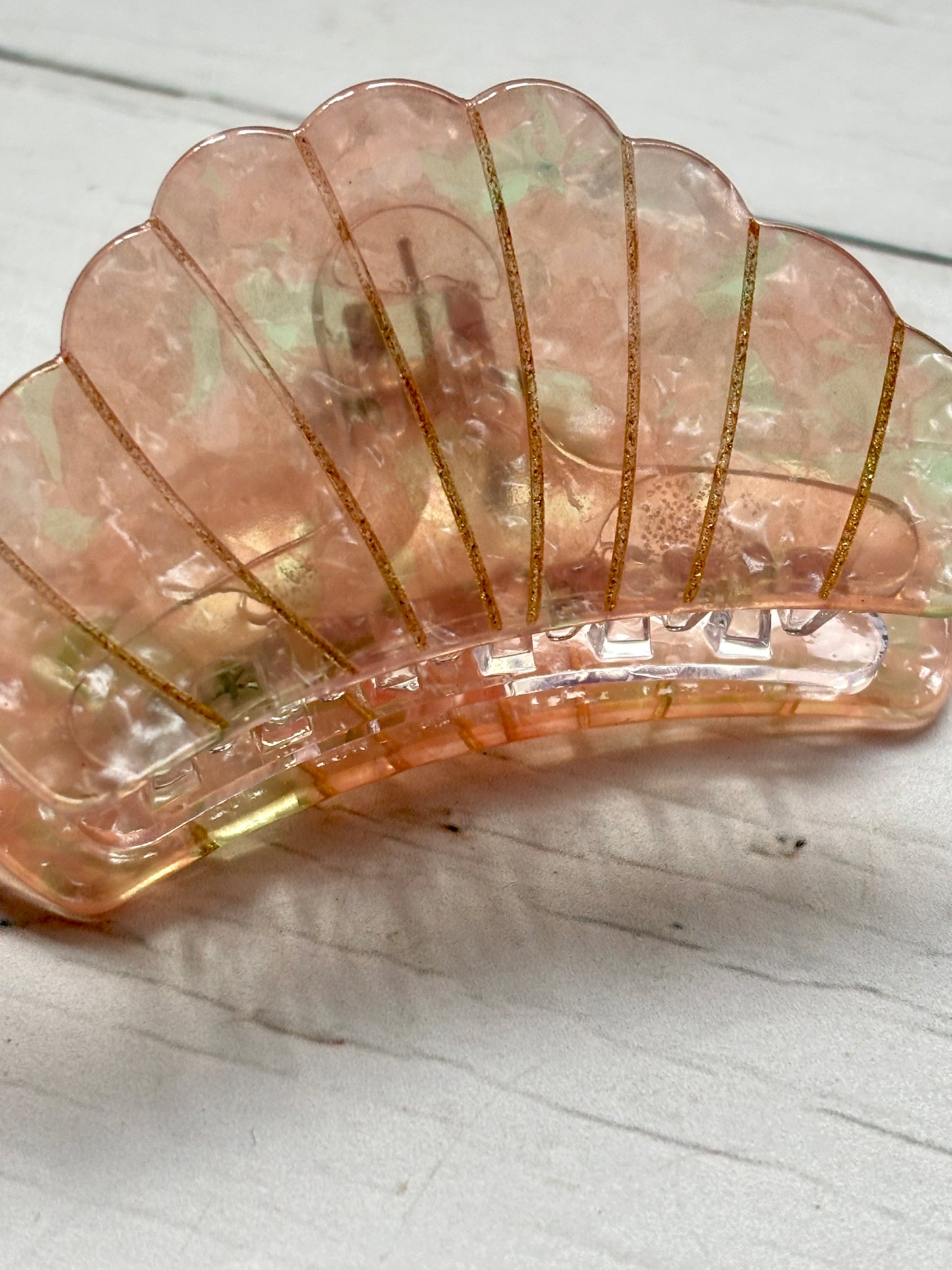 closeup shot of the scalloped edge and gripping teeth of the iridescent pink shell hair claw clip with gold glitter lines ocean accessory