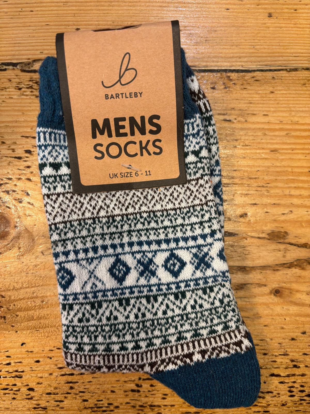 Colorful patterned Bartleby Men’s socks in teal, white, and green tones on wooden surface