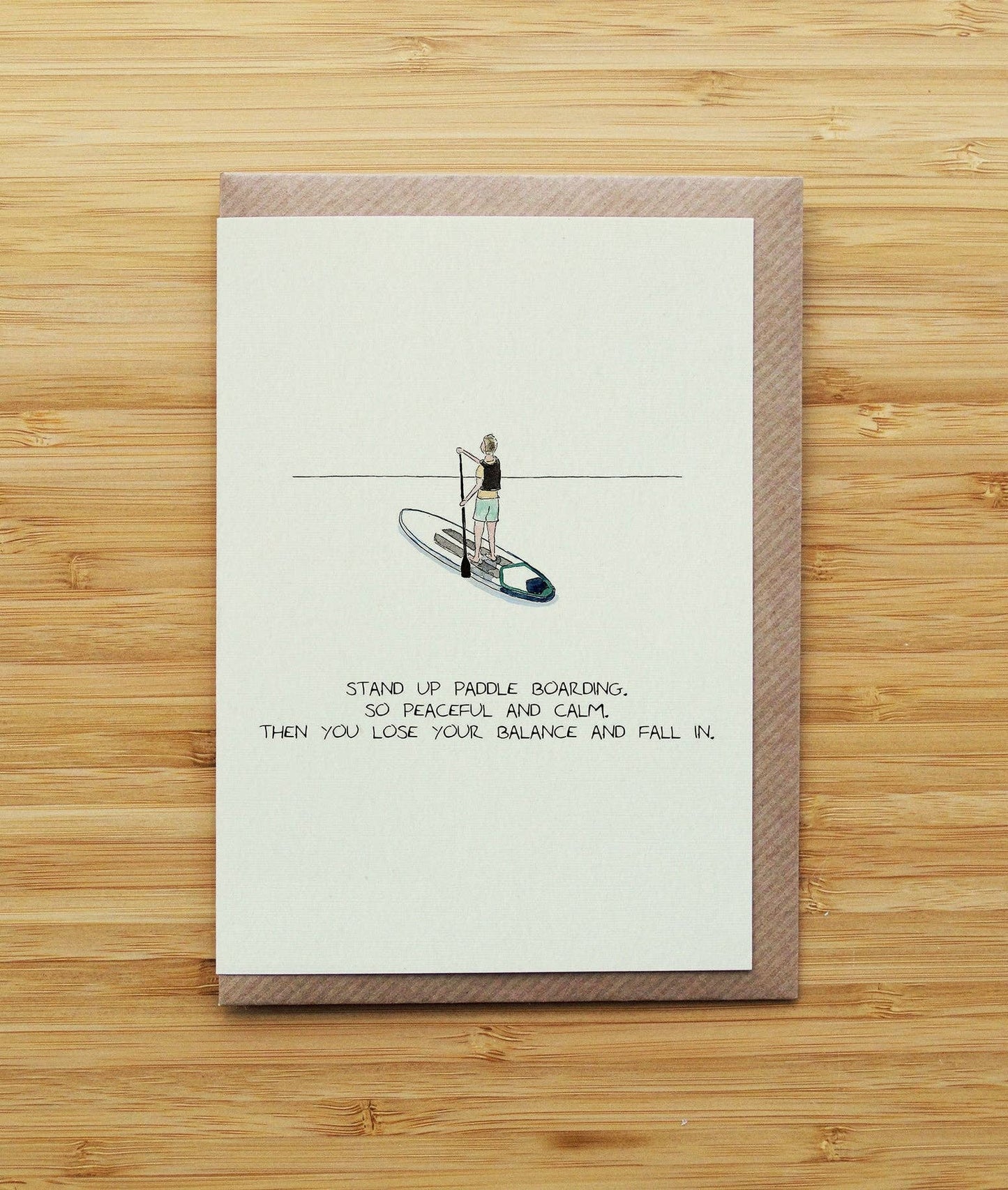greetings card with a stand-up paddleboard illustration and text on a wooden surface