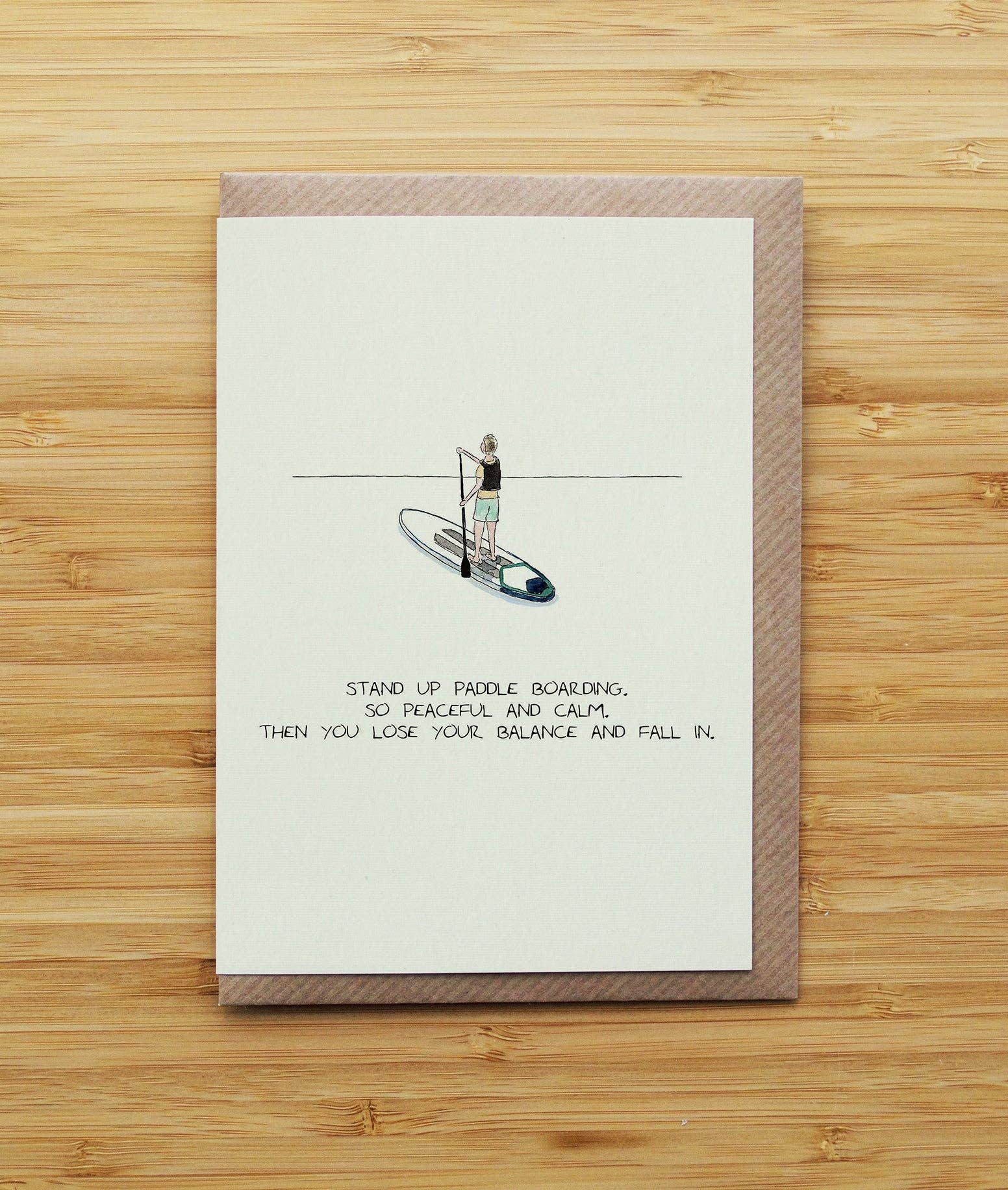greetings card with a stand-up paddleboard illustration and text on a wooden surface