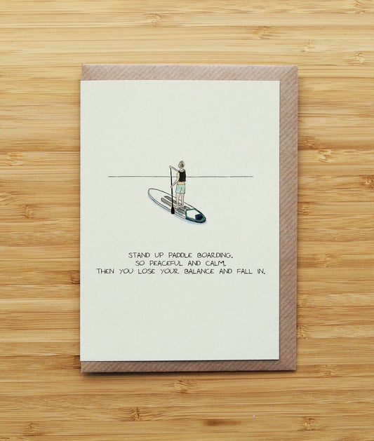 greetings card with a stand-up paddleboard illustration and text on a wooden surface