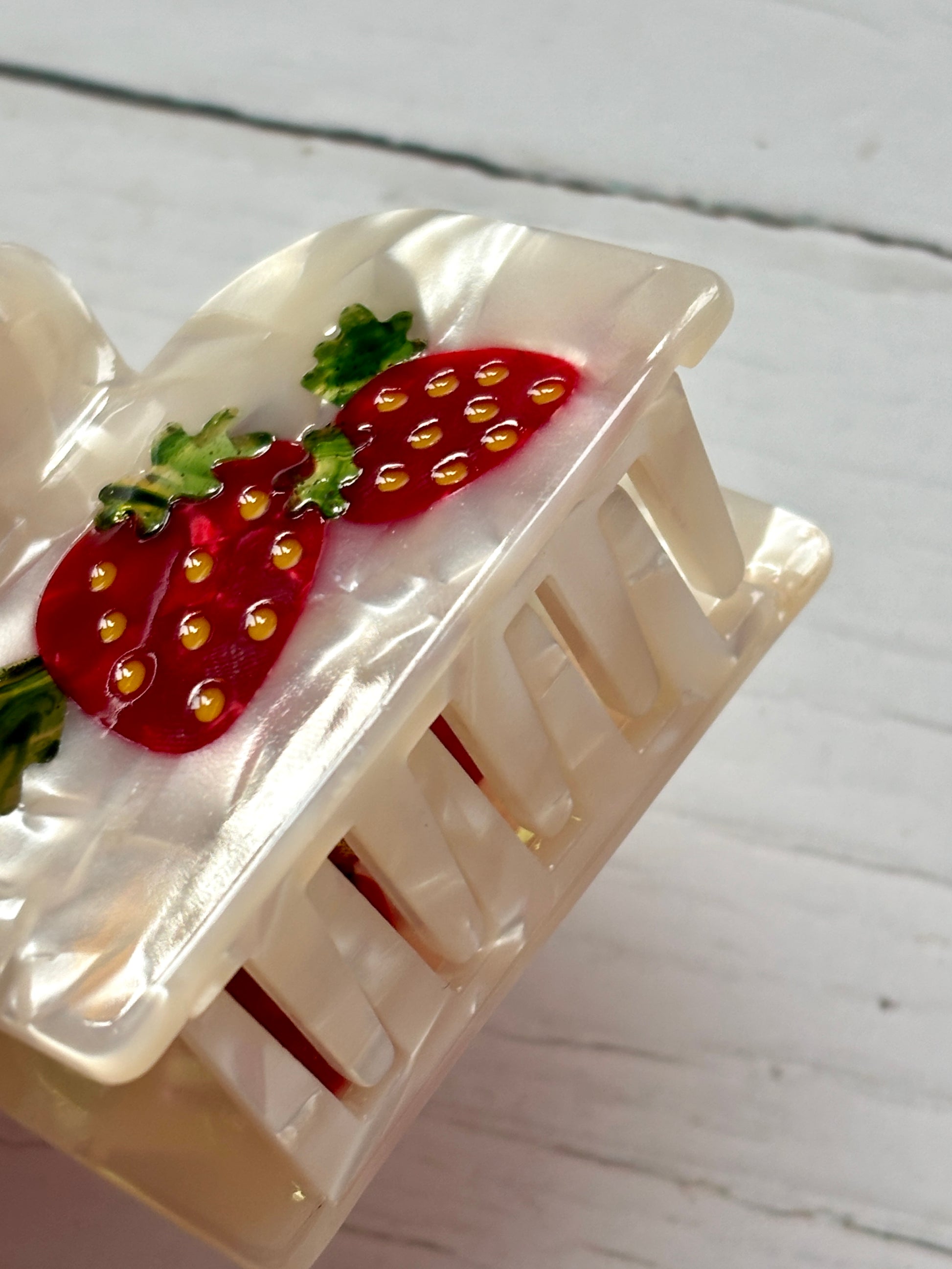 closeup shot of strawberries & cream hair claw—pearlescent clip with red berries, green leaves, and textured finish for sweet style