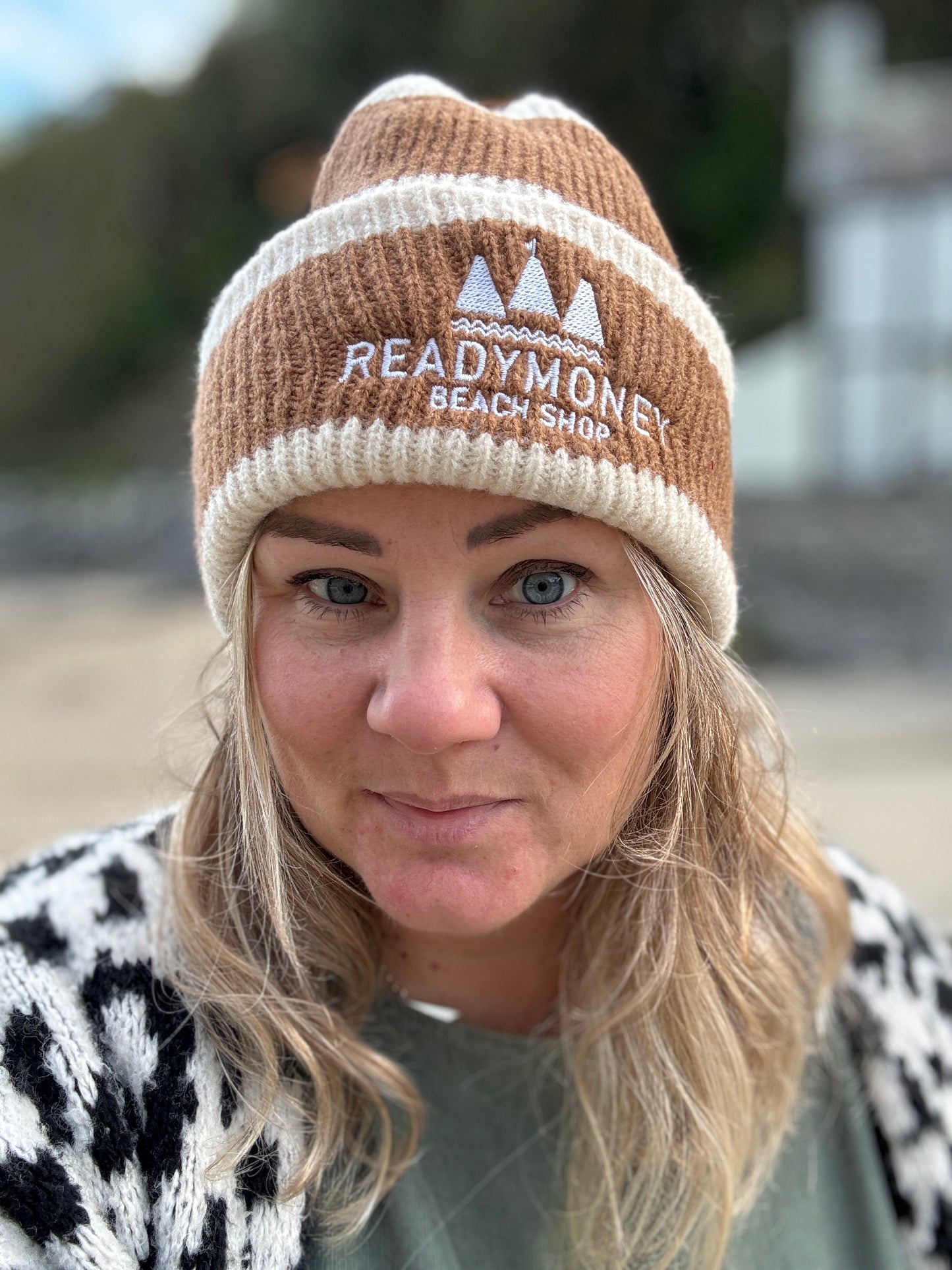 Readymoney Beach Shop beanie in cream and brown—cozy ribbed knit hat with coastal logo, styled for outdoor winter adventures