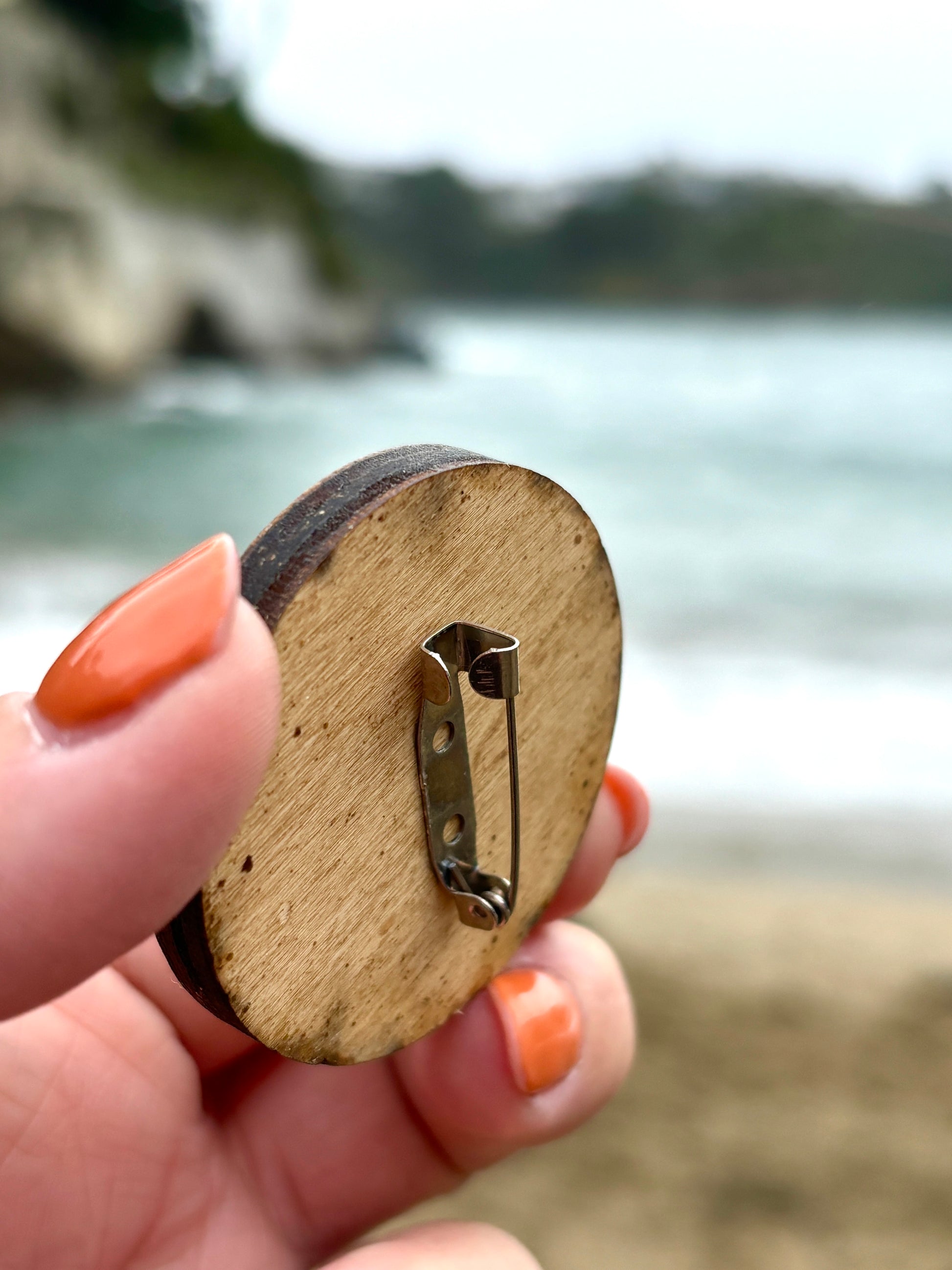 back view of 'Readymoney Cove Swim Club' wooden badge shows metal pin clasp, raw wood texture, coastal accessory, brooch gift
