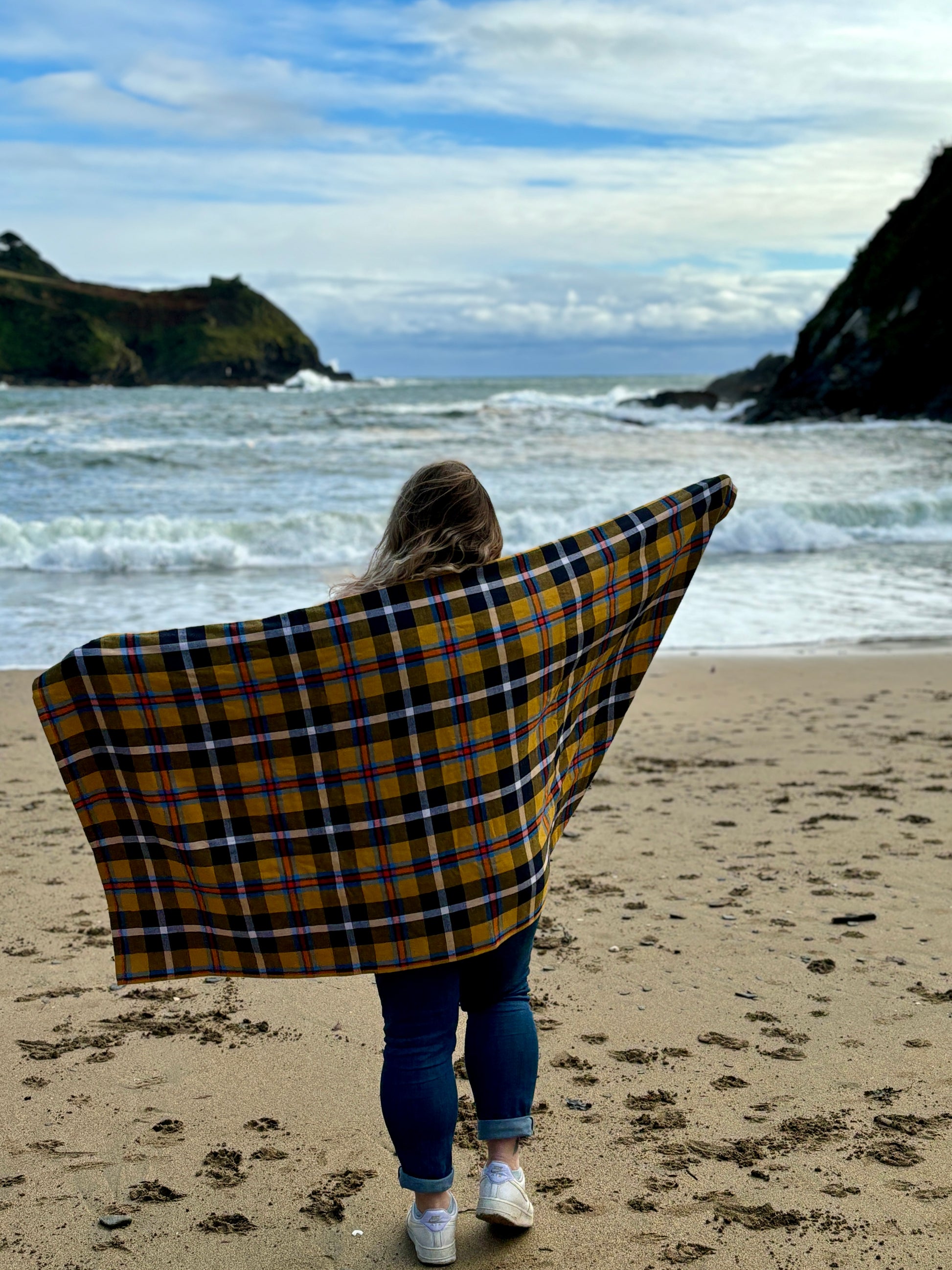 wind-resistant yellow tartan cotton beach blanket held by woman on a rugged coastline perfect for travel, beach, and outdoor adventures