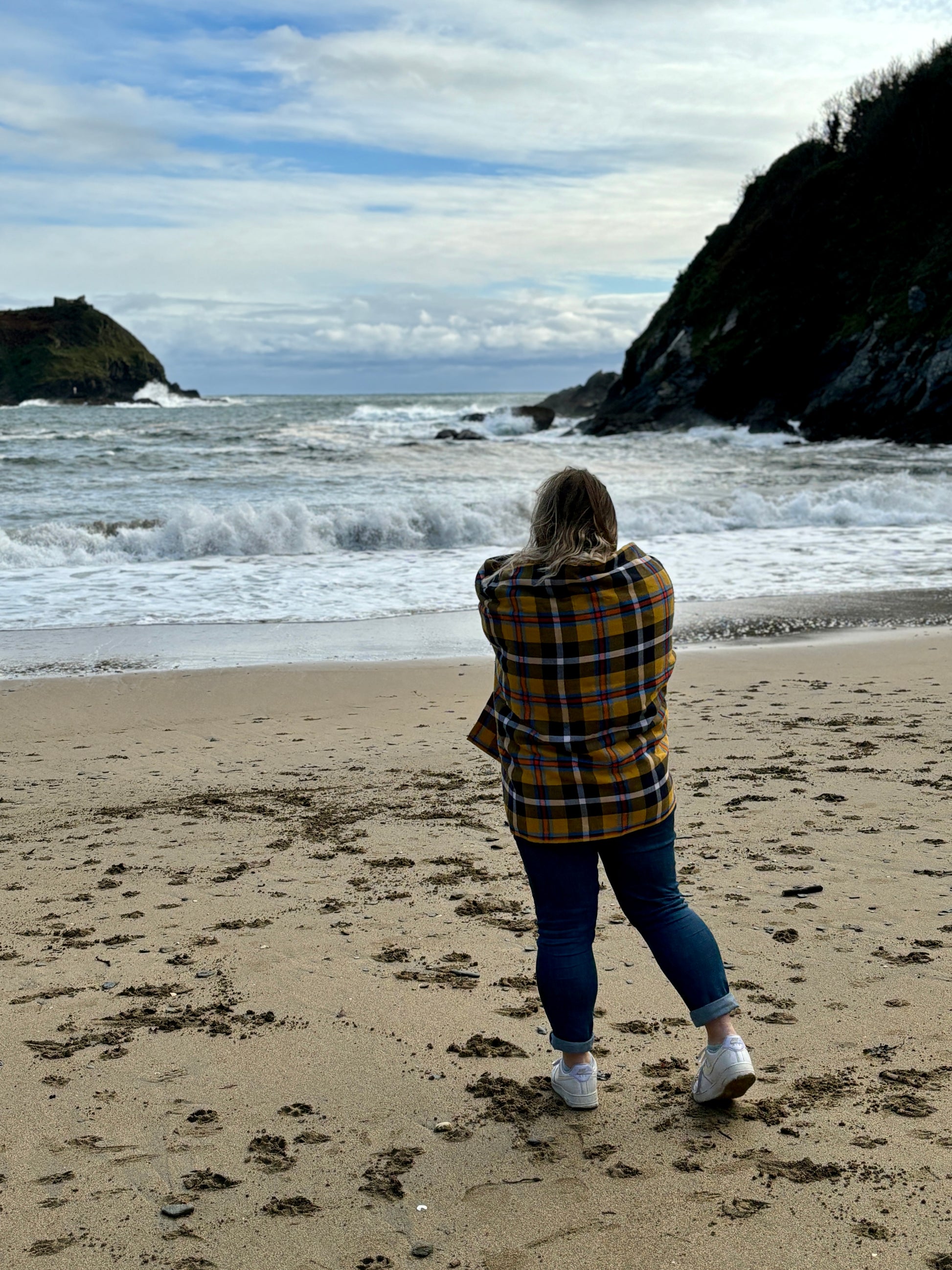 woman wrapped in a yellow tartan cotton beach towel on a sandy, rugged beach oversized blanket for travel, picnics, and coastal comfort