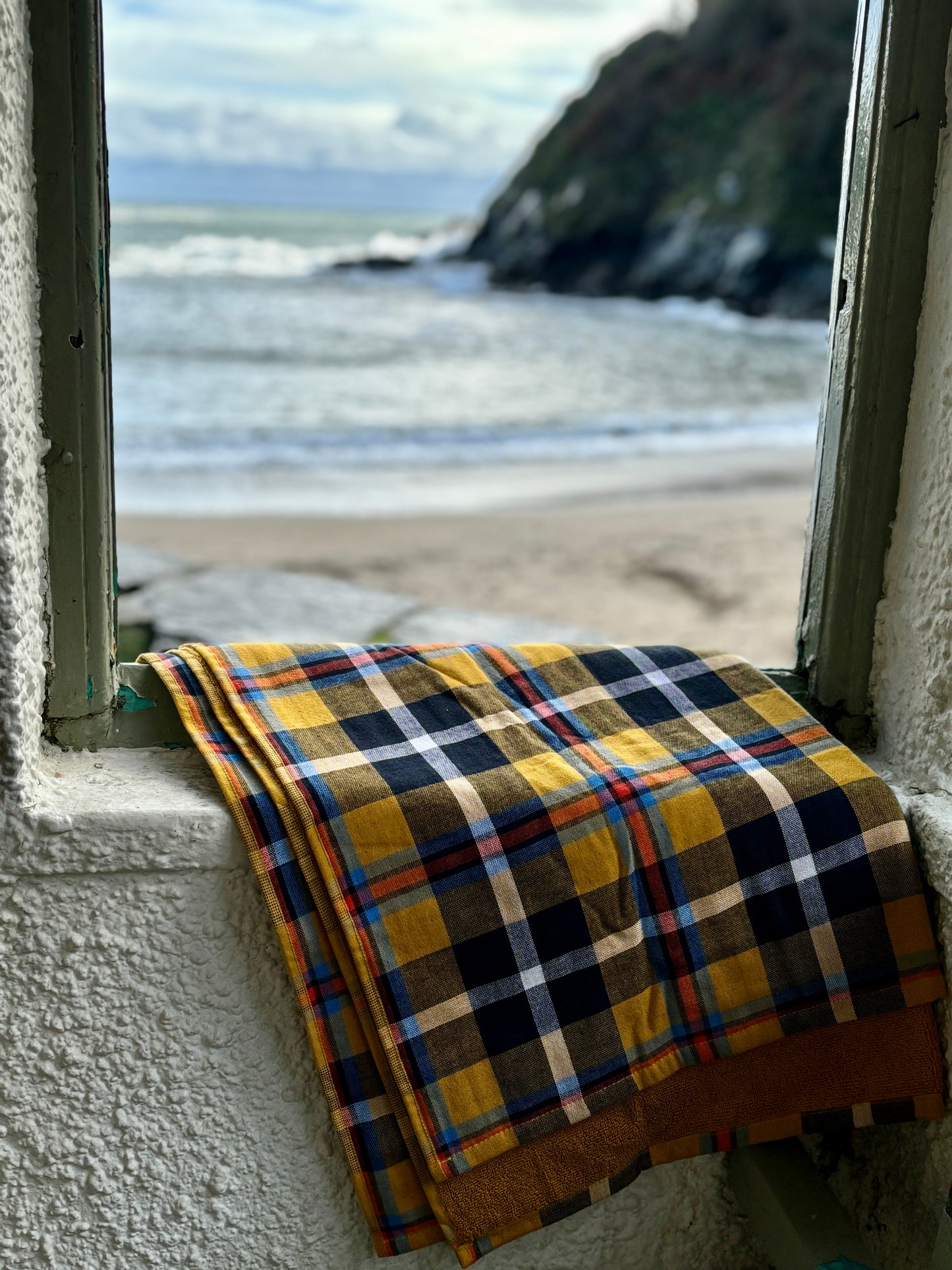 stylish yellow tartan cotton beach towel on a window sill with sea view oversized blanket for summer travel or picnics