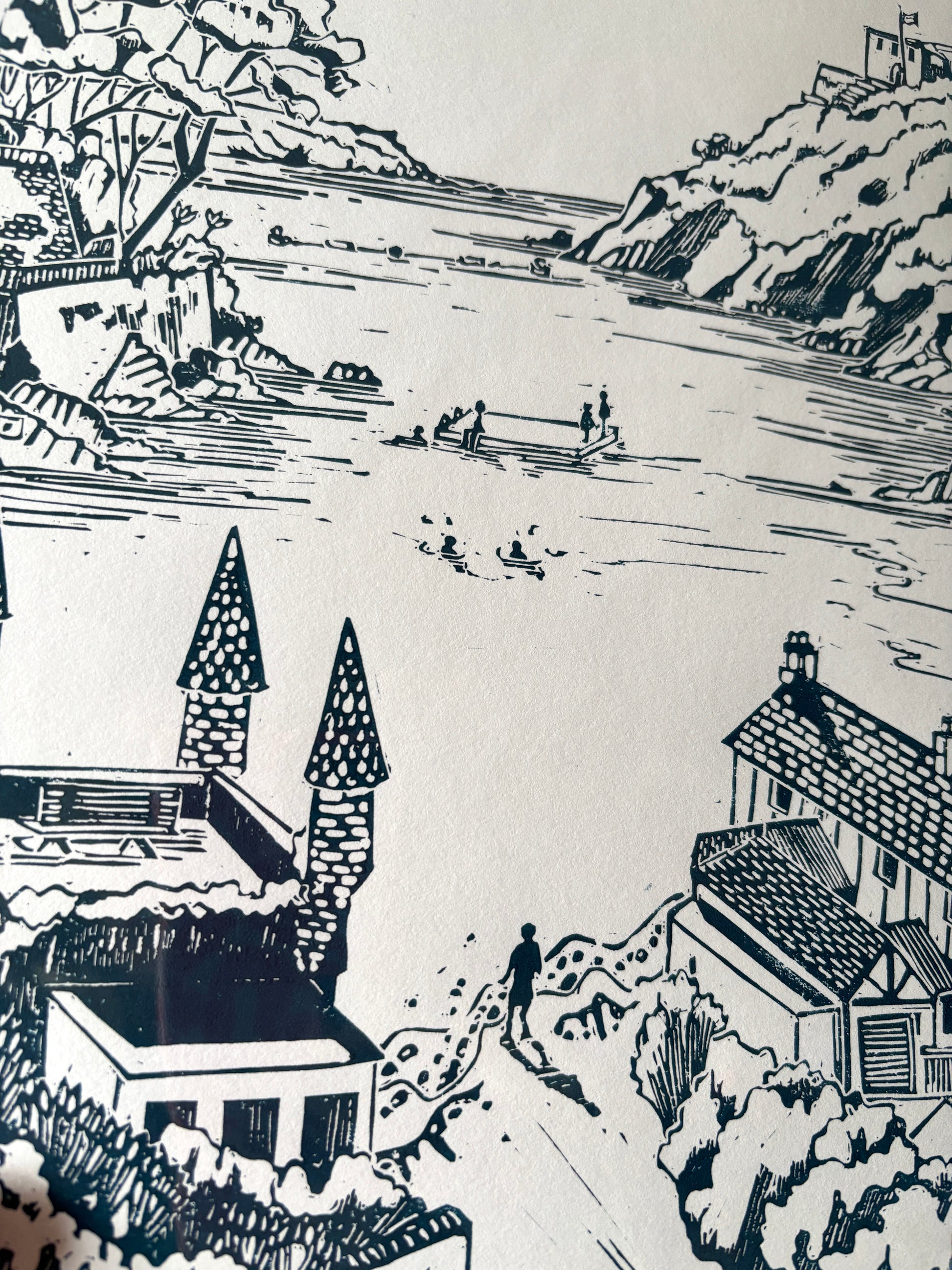 closeup shot of a detailed linocut print showing a Cornish bay, cottages, and sea activity. Original green coastal wall art