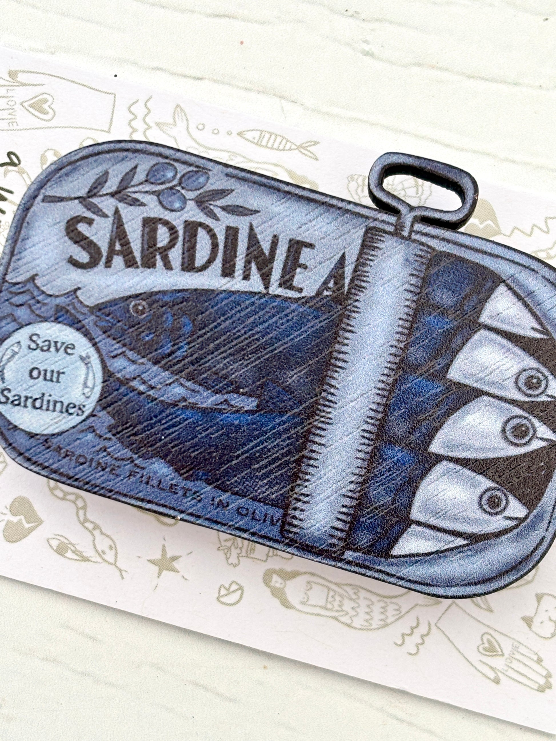 closeup shot of tin of sardines wooden pin—eco-friendly nautical badge with quirky fish tin design for ocean lovers and coastal gifting