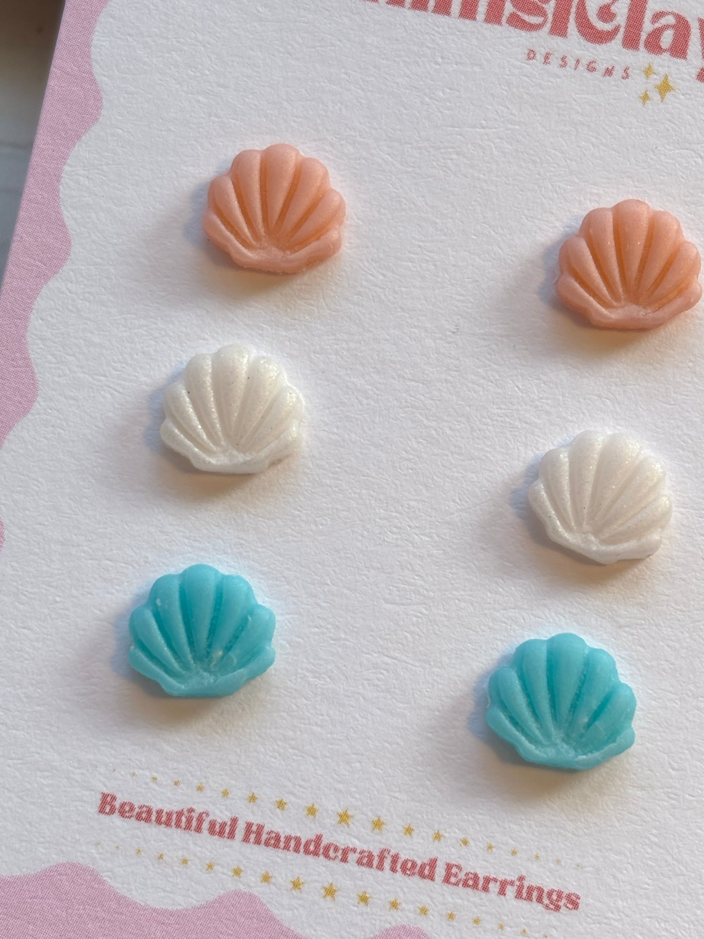 closeup shot of triple sea shell stud earrings pastel pink, white, and blue handmade polymer clay jewelry beach gift