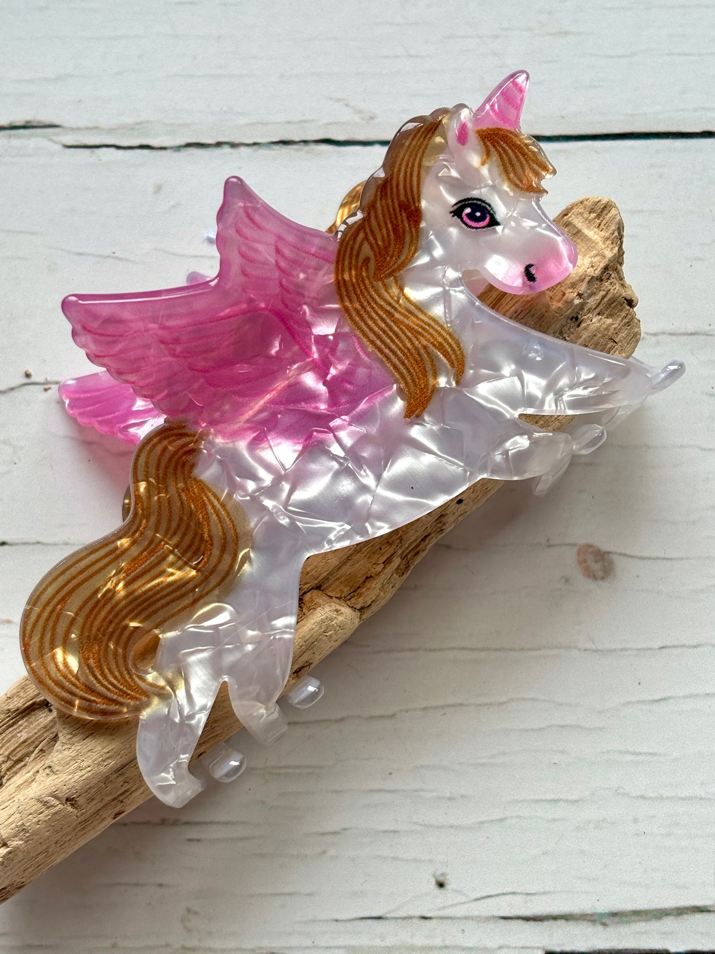 marbled pearlescent unicorn with pink wings and gold mane/tail hair claw clip funky Pegasus novelty accessory on driftwood