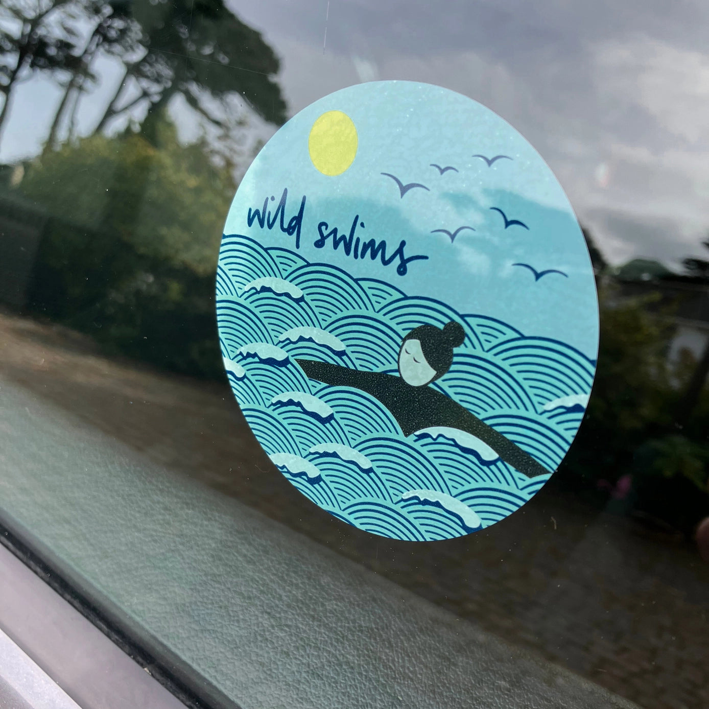 wild swims car sticker on window with ocean waves, swimmer, sun, and birds—ideal for nature swim enthusiasts