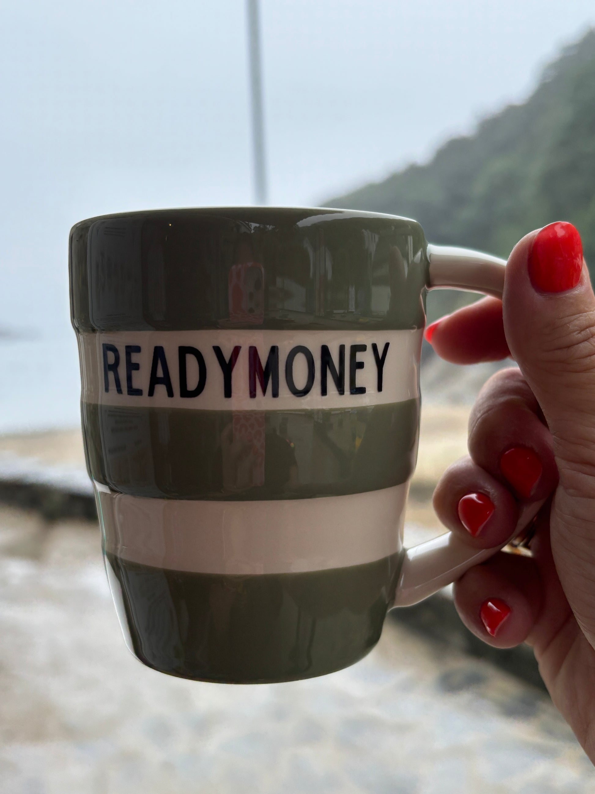 green striped READYMONEY ceramic mug held at beach - 12oz coastal coffee cup with ocean view background