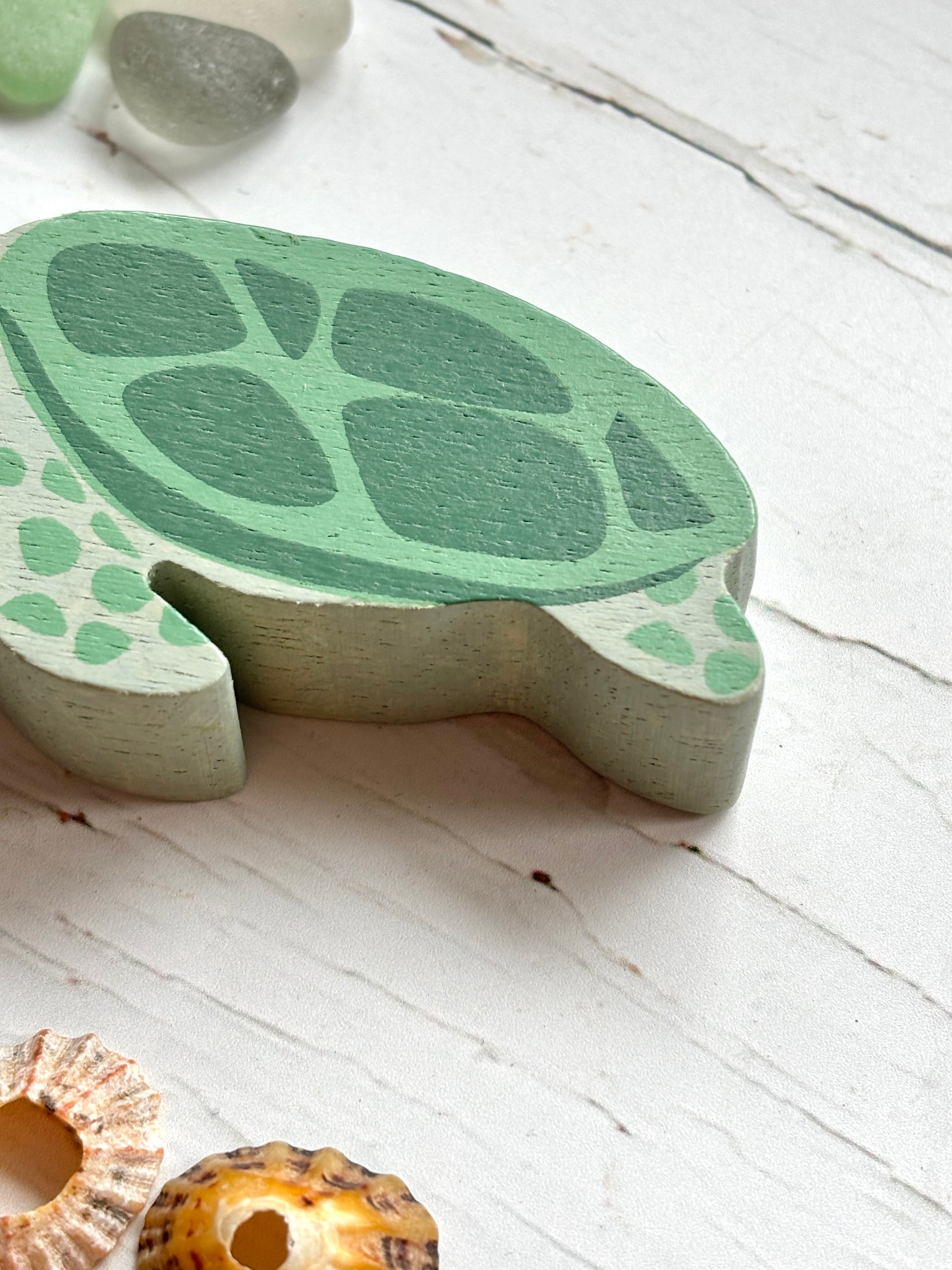 closeup shot of wooden sea turtle tail with green shell detail, hand-painted coastal toy for beach-themed decor