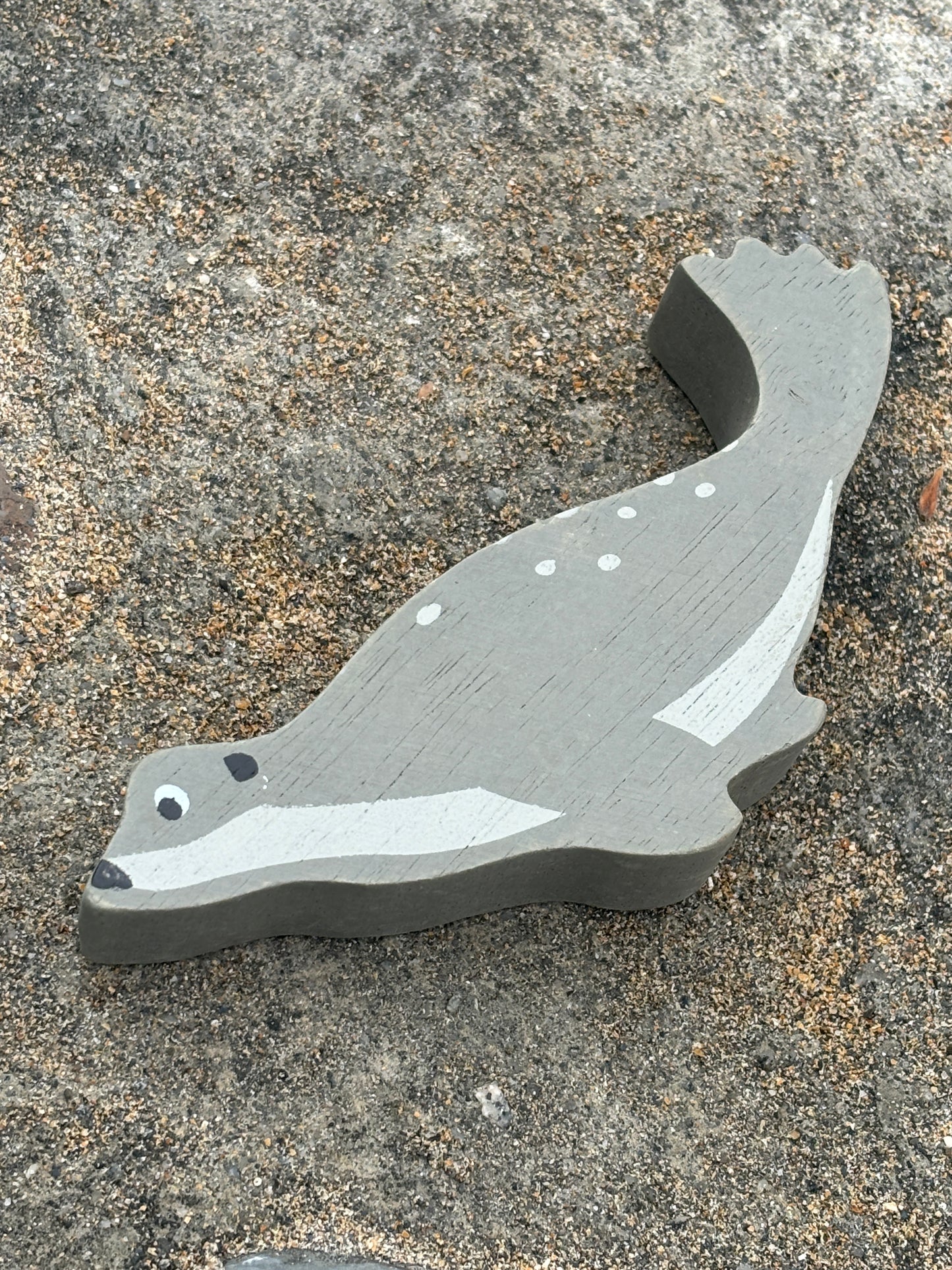gray wooden seal toy with white spots, handcrafted coastal animal decor styled on textured stone for beach lovers