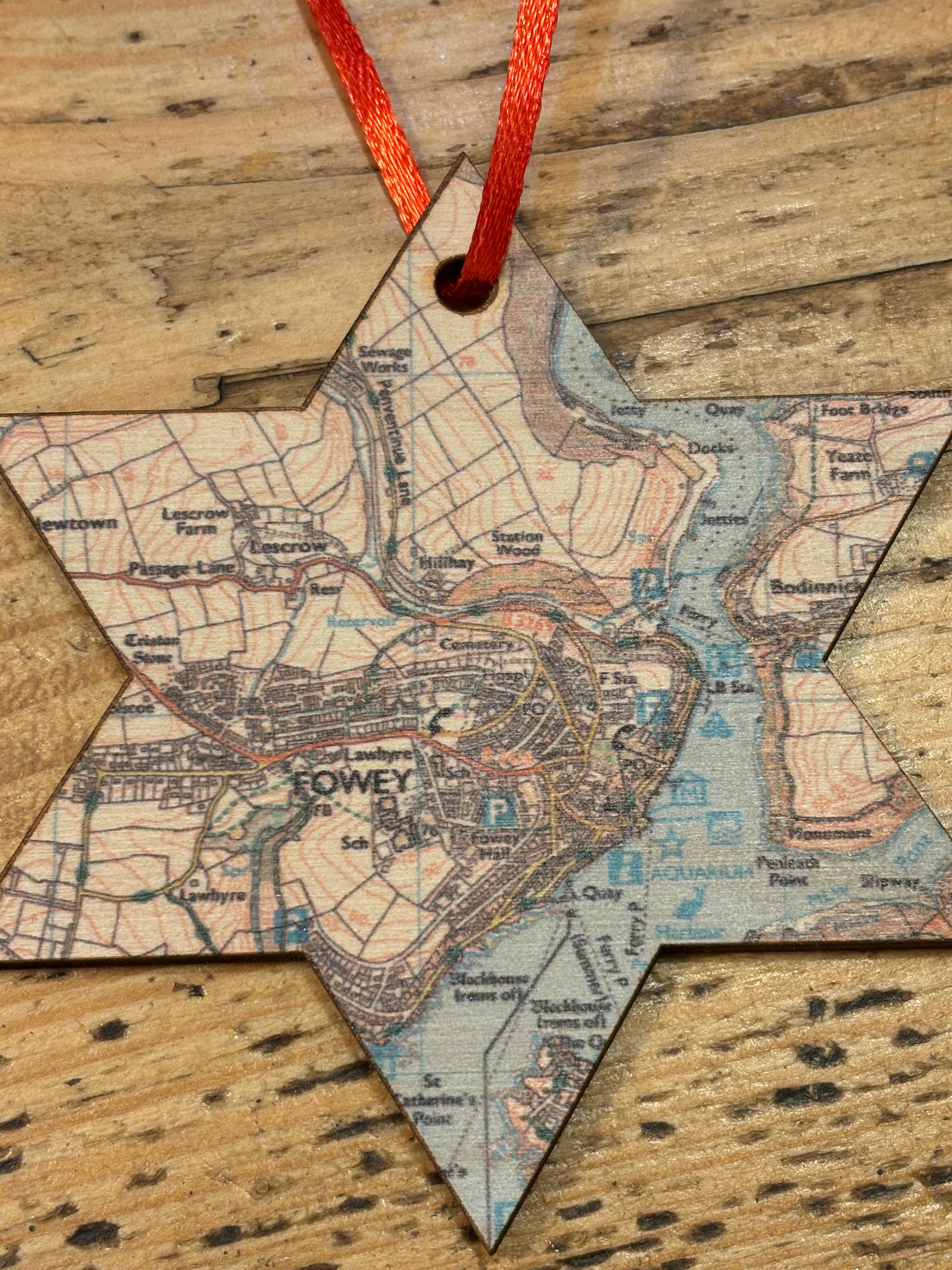 Star-shaped christmas decoration featuring a map of Fowey with a red ribbon on a wooden surface