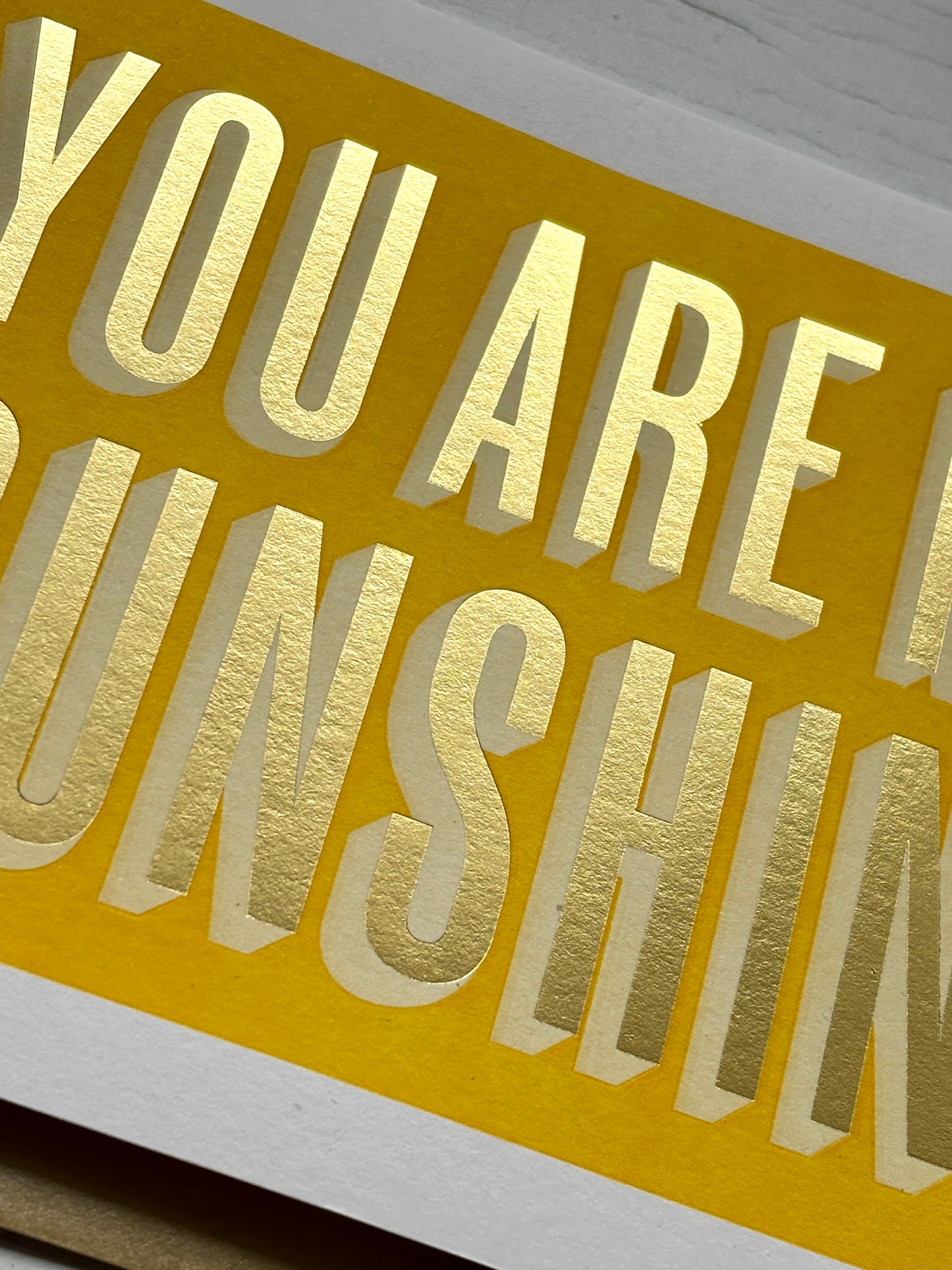 closeup shot of sunshine card with gold embossed text on vibrant yellow, perfect for joyful gifting and coastal-inspired love notes