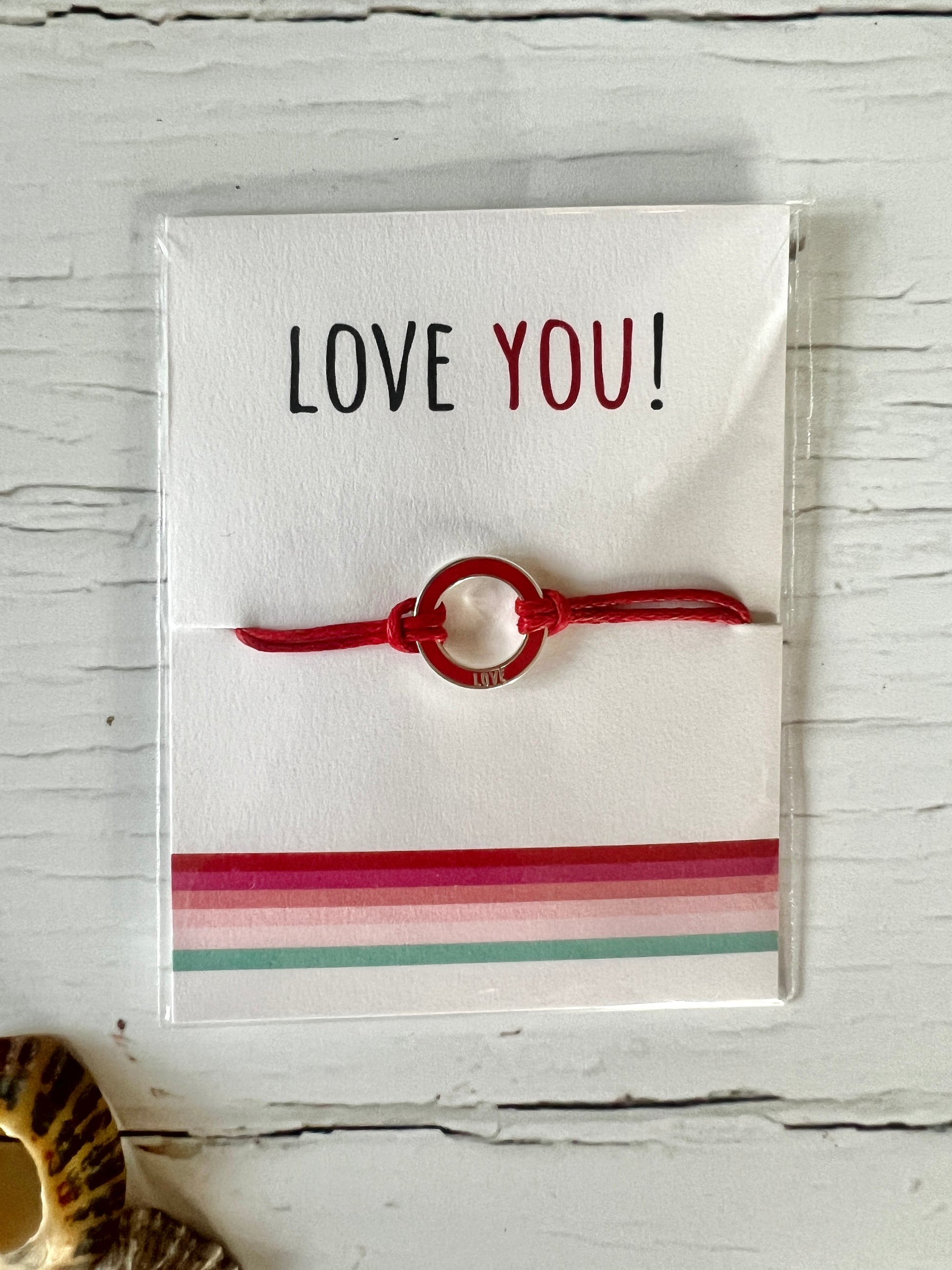 A Valentine's string bracelet with a red cord and a red enamel disc charm . The packing card says Love You