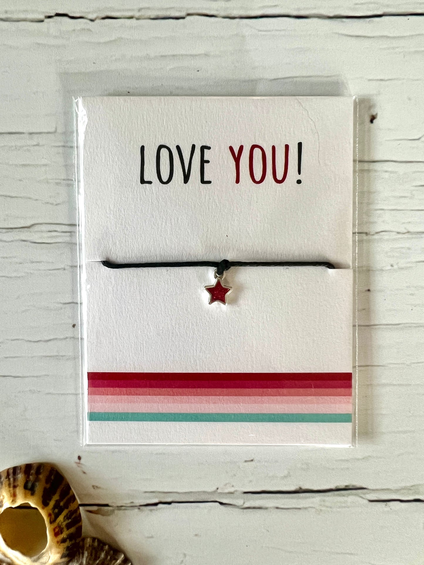 A Valentine's string bracelet with a black cord and a red glittery enamel star shaped charm . The packing card says Love You